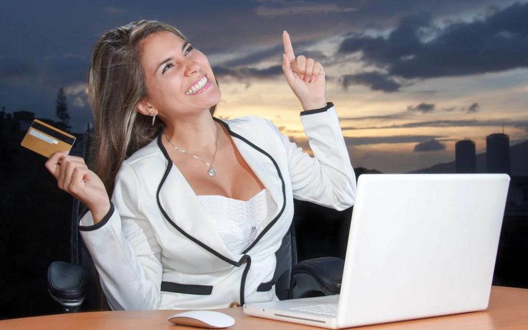 An excited woman holding a credit card at her computer